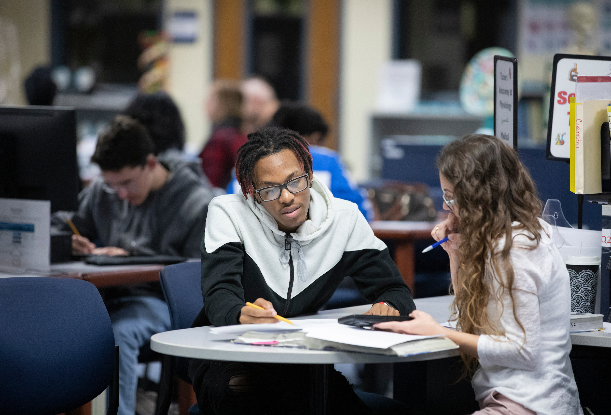 A tutor and student gather around a table and review a book in the library.