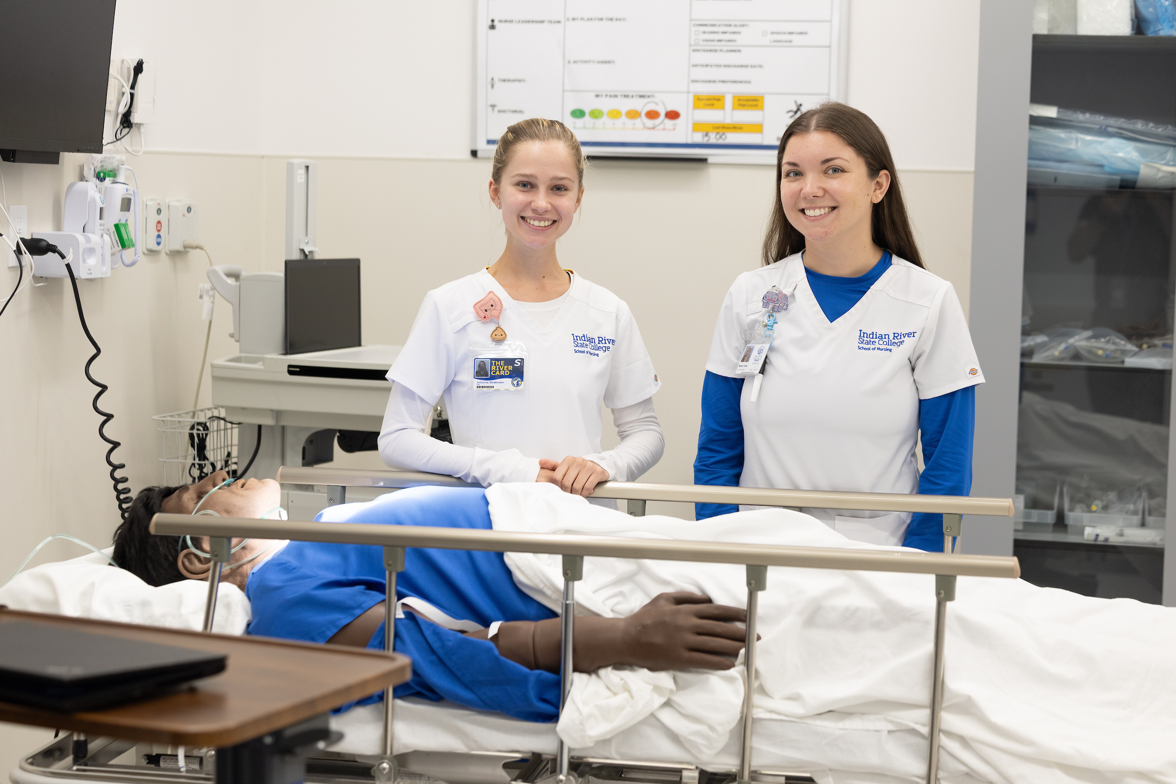 In a hospital-like setting, two nursing students stand at the bedside of a simulated patient at the Indian River State College School of Nursing.