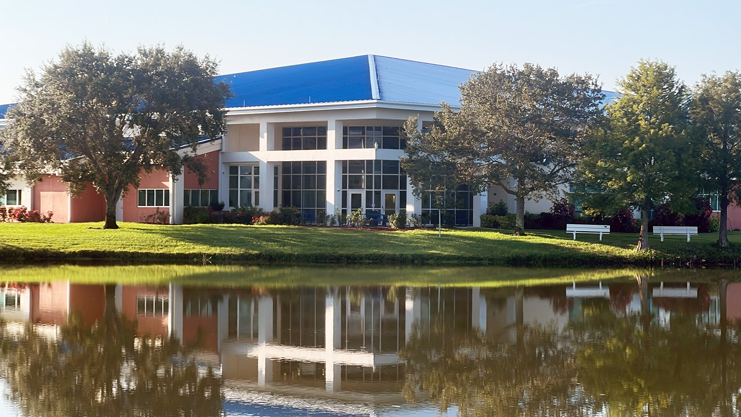 The Clark Advanced Learning Center is a two-story building with a blue roof and trees by a lake.